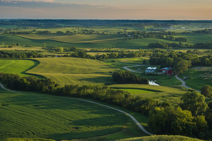 About Our Agency - Aerial View of the Wisconsin Countryside Displaying Farmlands, a Creek and a Farm With Small Valleys in the Distance During Sunrise